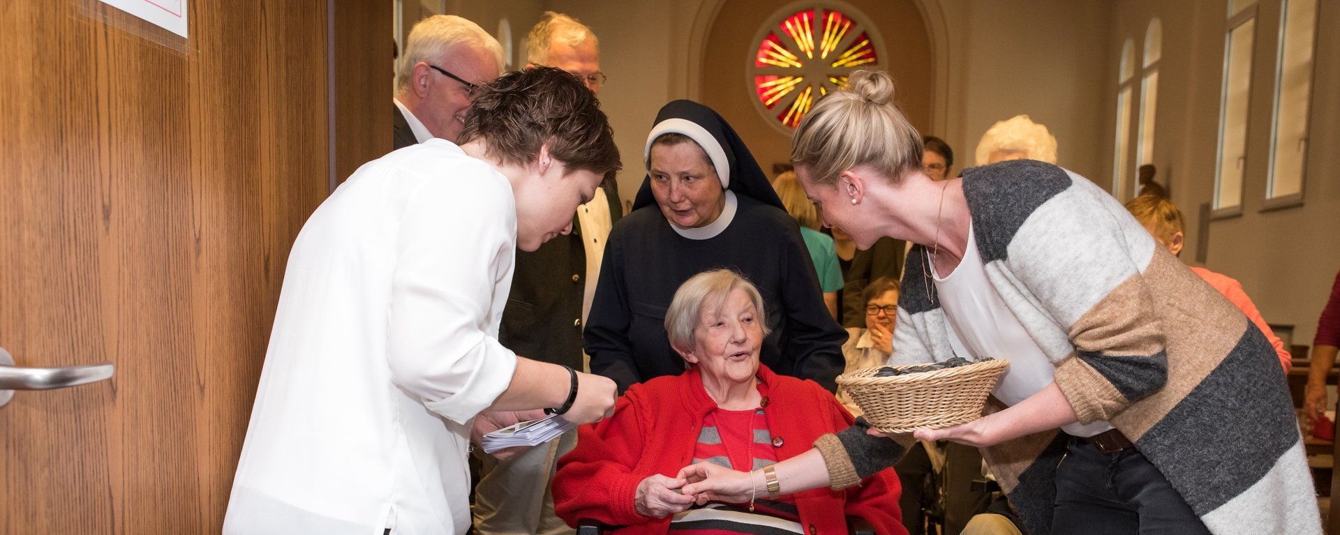 In der Kirche: eine Frau im Rollstuhl wird von einer Schwester zum Ende der Messe hinausgeschoben