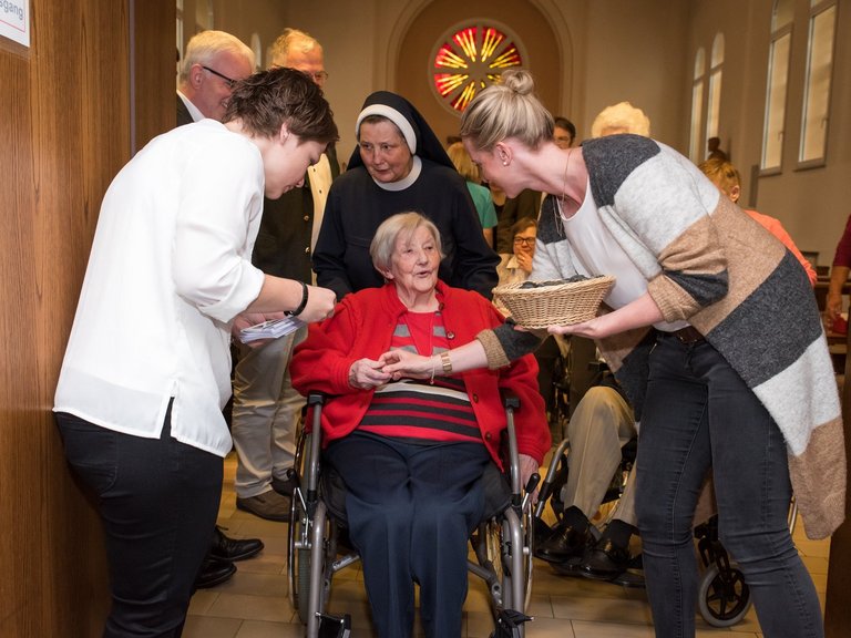 In der Kirche: eine Frau im Rollstuhl wird von einer Schwester zum Ende der Messe hinausgeschoben