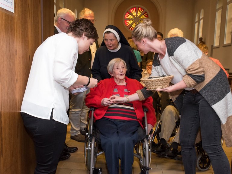 In der Kirche: eine Frau im Rollstuhl wird von einer Schwester zum Ende der Messe hinausgeschoben