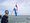 Ein lächelnder Mann mit blauer Sonnenbrille hält auf einem Boot eine niederländische Flagge. Im Hintergrund ist das offene Wasser unter einem bewölkten Himmel zu sehen.