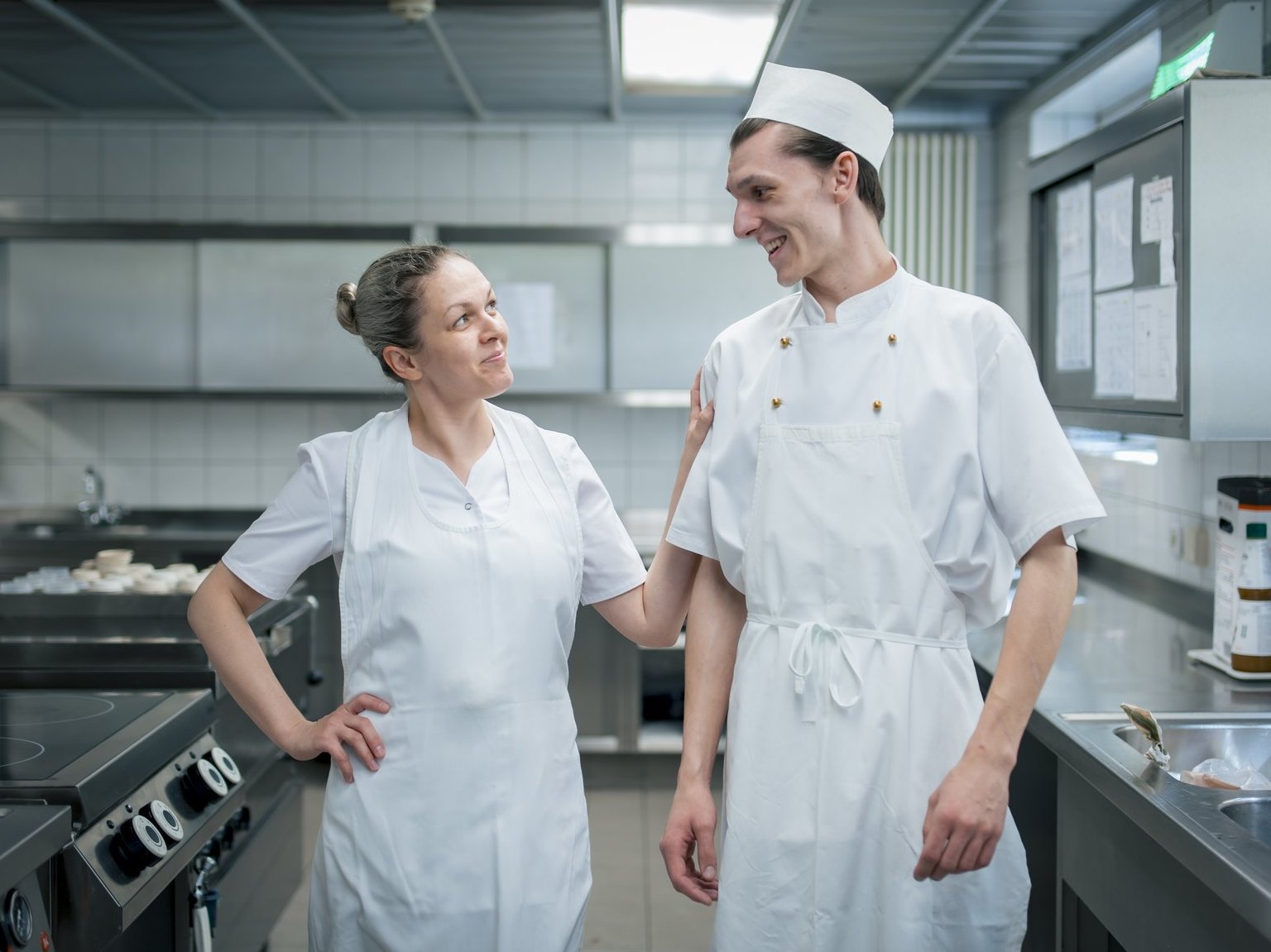 Zwei Mitarbeitende des Küchenteams stehen in der Küche und lachen sich an.