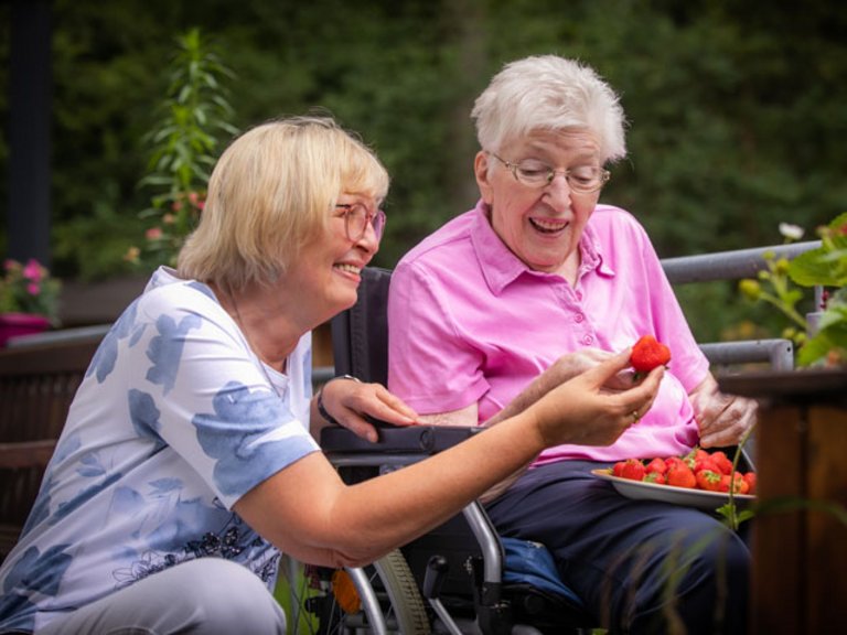 Pflegerin isst mit einer Heimbewohnerin Erdbeeren