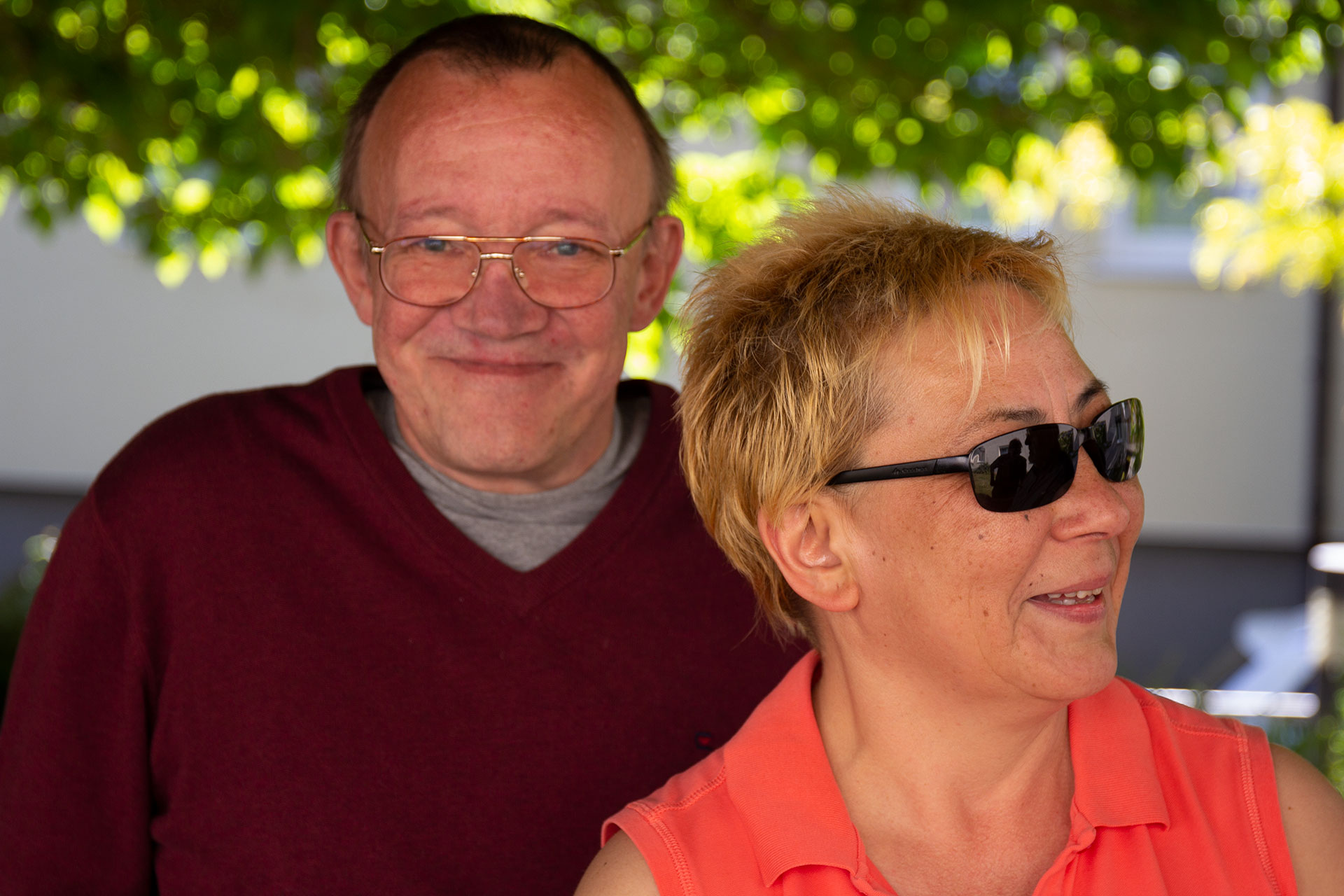 Portrait: eine Frau mit sehr dunkler Sonnenbrille - dahinter ein Mann